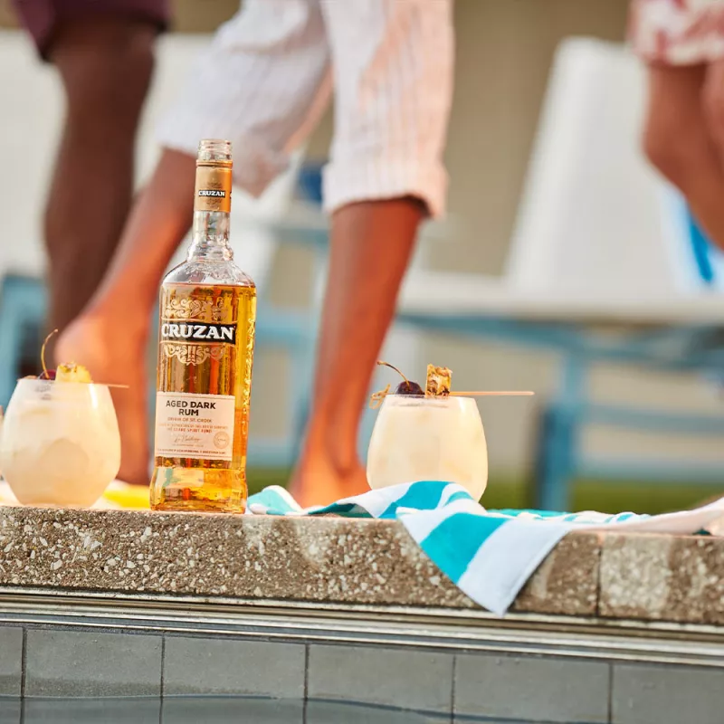 Image of two piña coladas in clear glasses with a bottle of Cruzan® Aged Dark Rum outside.