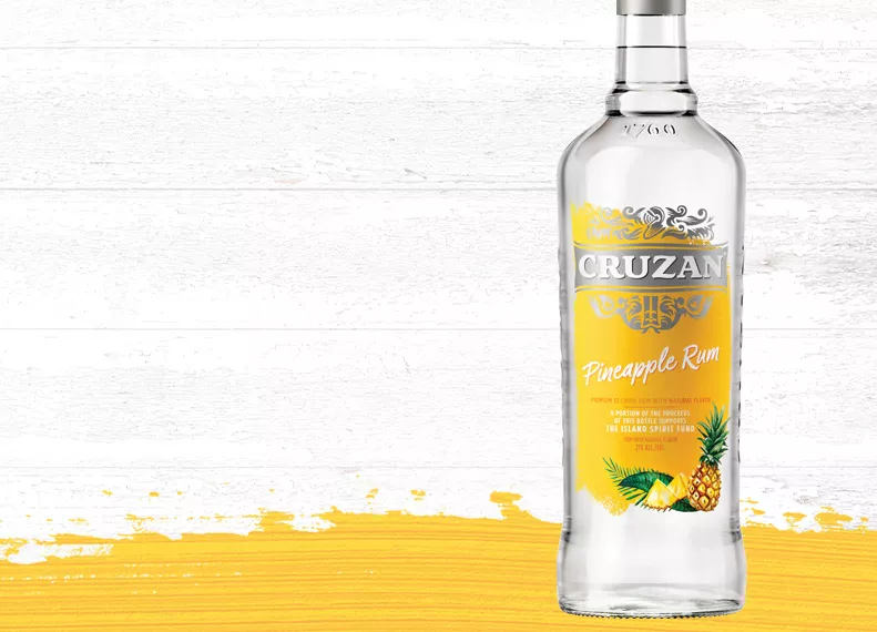 Cruzan Pineapple Rum glass bottle with a yellow label with a whitewashed wood background with a pineapple yellow paint swash.