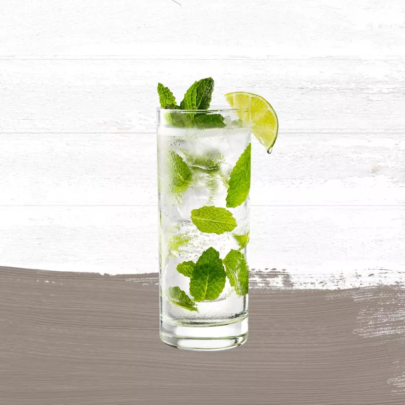 Mojito in a tall clear glass, garnished with a lime wedge and mint set against a whitewashed wood background with a taupe paint swash.