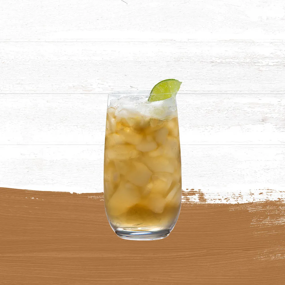 Stormy Weather cocktail in a tall cocktail glass, garnished with a lime wedge set against a whitewashed wood background with a gold paint swash.