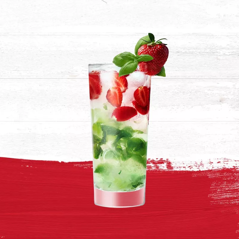 Cruzan® Strawberry Basil Smash cocktail in a tall clear glass mixed with basil and sliced strawberries set against a whitewashed wood background with a red paint swash.