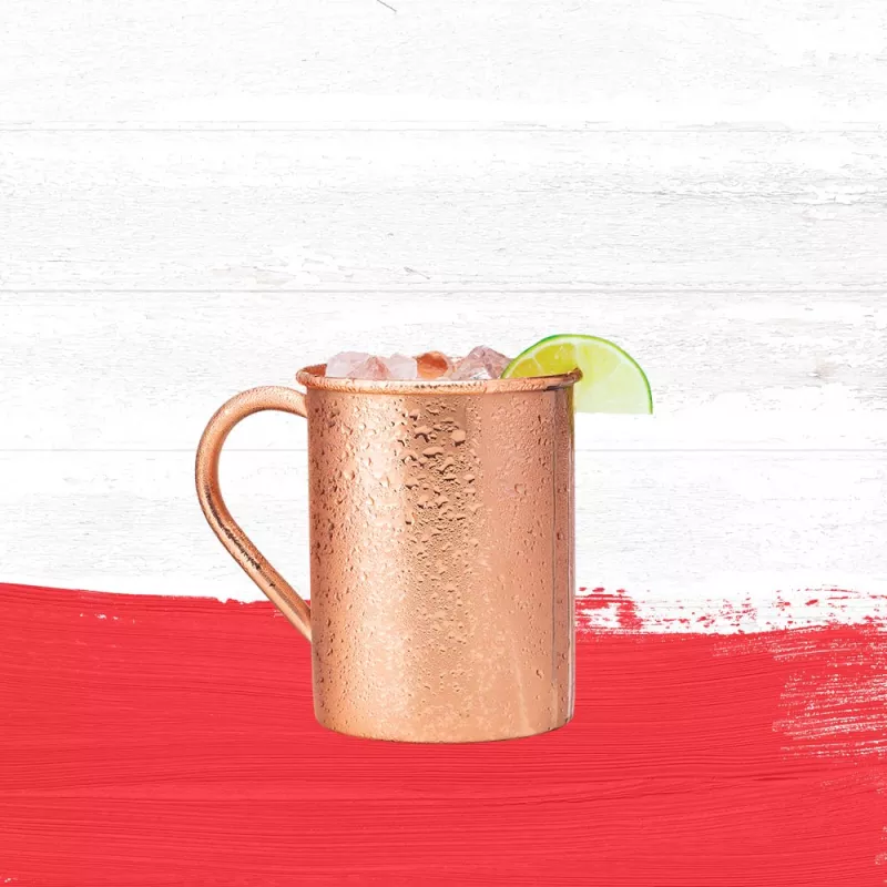 Undertow cocktail in a copper mule mug, garnished with a slice of lime against a whitewashed wood background with a dark orange paint swash.