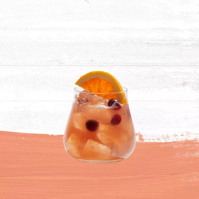 Cruzan® Island Breeze cocktail garnished with citrus fruit and cranberries in a short glass set against a whitewashed wood background with a peach paint swash.