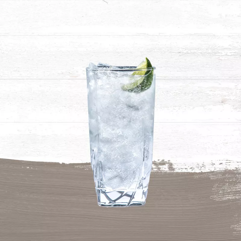 Cruzan® Aged Light & Tonic made with Cruzan® Aged Light Rum in a tall, clear glass garnished with a lime wedge set against a whitewashed wood background with a taupe paint swash.