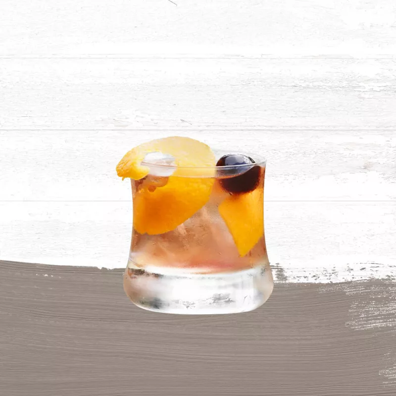 Cruzan® Morning cocktail, a light rum drink, in a rocks glass garnished with an orange peel and a black cherry set against a whitewashed background with a taupe paint swash.