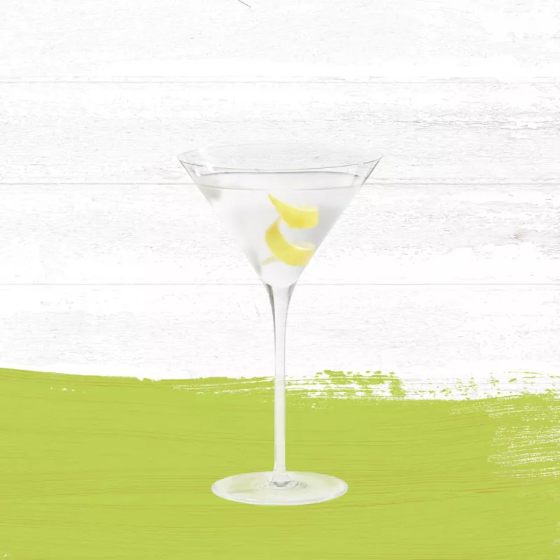 Guava Sidecar cocktail served in a clear martini glass garnished with a lemon twist against a whitewashed wood background with a lime green paint swash.