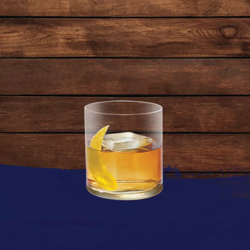 Rum old fashioned cocktail set against an oak barrel panel background with a navy blue paint swash.