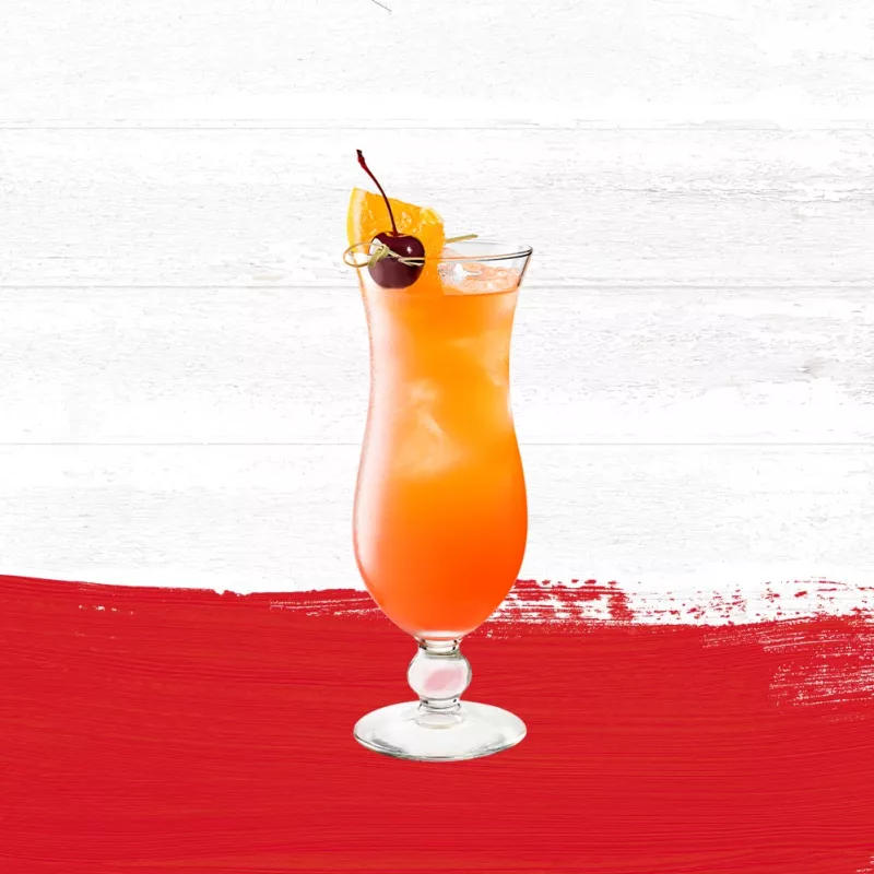 Hurricane drink in a clear glass garnished with a cherry and pineapple set against a whitewashed wood background with a red paint swash.