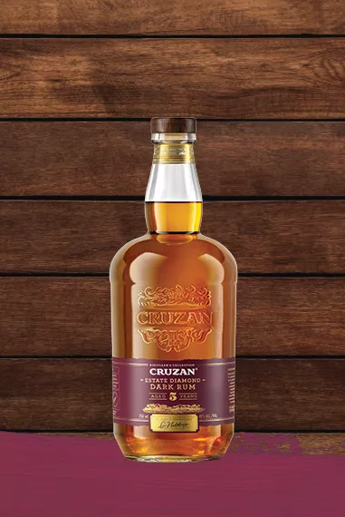 Cruzan Estate Diamond Dark Rum in a glass bottle set against dark oak wood panels with a maroon paint swash.