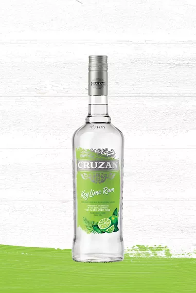 Cruzan Key Lime Rum clear glass bottle with a lime green label adorned with limes set against a whitewashed wood background with a lime green paint swash.