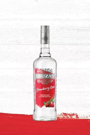 Cruzan Strawberry Rum clear glass bottle with a red label adorned with ripe strawberries set against a whitewashed wood background with a red paint swash.