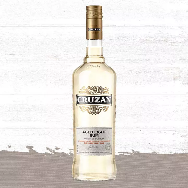 Image of a glass bottle of Cruzan Aged Light Rum against a background of light oak barrel panels and a gray-taupe paint smudge.