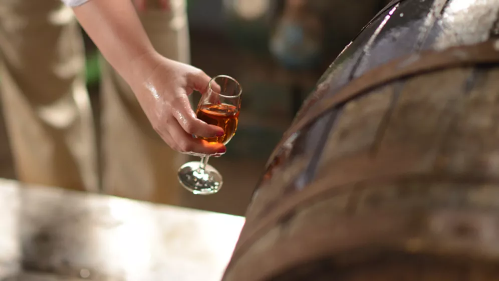 Image of a person holding a glass of Cruzan® Rum next to an oak barrel.