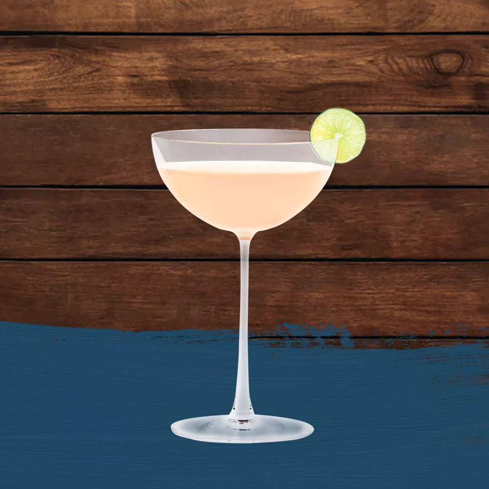 Hemingway Daiquiri in a coupe glass, garnished with a lime wheel set against a wood background with a dark blue paint swash.