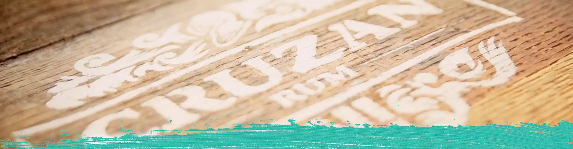 Image of Cruzan Aged Light Rum, Cruzan Single Barrel Rum, and Cruzan Coconut Rum against a background of white oak panels with a turquoise paint smudge and the Cruzan Rum logo.