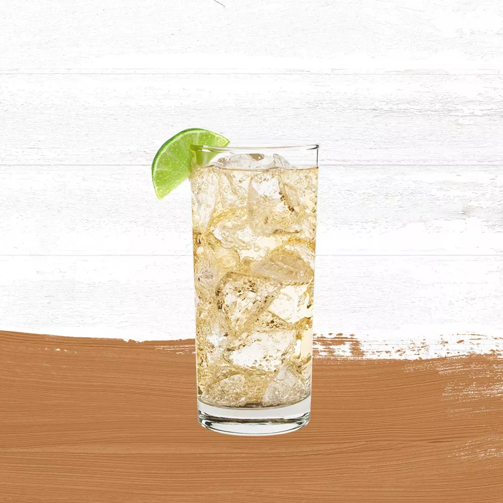 Cruzan® Aged Dark Rum and soda water in a tall clear glass garnished with a lime wedge set against a whitewashed wood background and a gold paint swash.