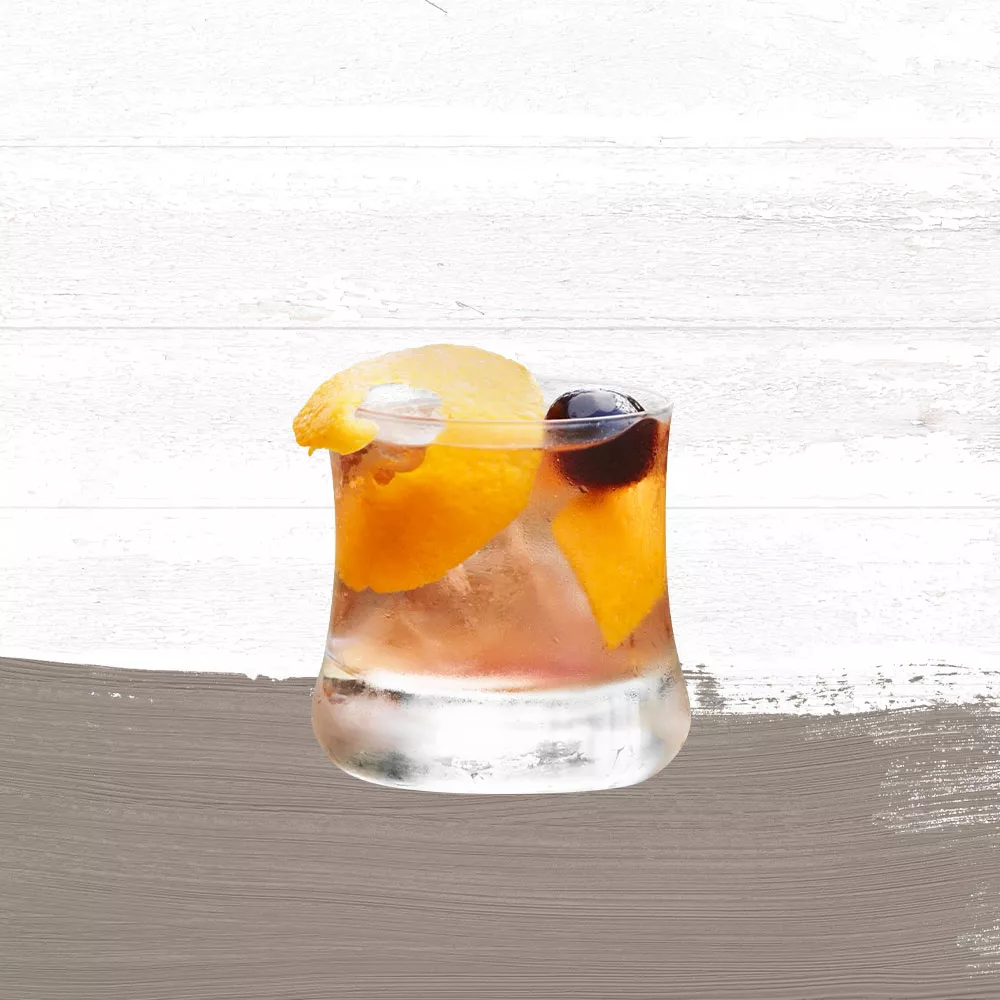 Cruzan® Morning cocktail, a light rum drink, in a rocks glass garnished with an orange peel and a black cherry set against a whitewashed background with a taupe paint swash.