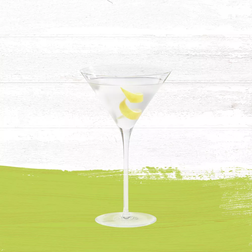 Guava Sidecar cocktail served in a clear martini glass garnished with a lemon twist against a whitewashed wood background with a lime green paint swash.